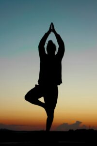 Yoga Asana stehender Baum macht Frau bei Sonnenuntergang für das Wurzelchakra.